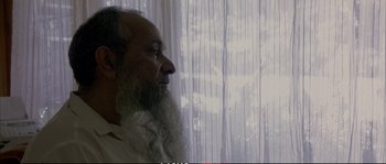 Movie still from “A Mighty Heart” (2007), directed by Michael Winterbottom – An older man with long white beard looking out a window; Close Up shot, Low angle