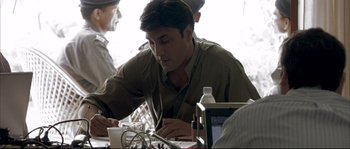 Movie still from “A Mighty Heart” (2007), directed by Michael Winterbottom – A man sitting at a table writing on a piece of paper; Medium shot, Over the shoulder angle