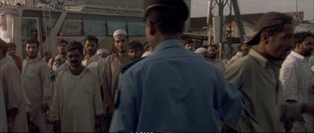 Movie still from “A Mighty Heart” (2007), directed by Michael Winterbottom – A group of men standing around a man in front of a building; Medium shot, Over the shoulder angle