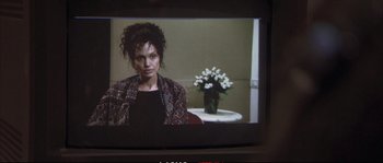 Movie still from “A Mighty Heart” (2007), directed by Michael Winterbottom – A woman sitting in front of a table with flowers on top of it; Close Up shot, Over the shoulder angle