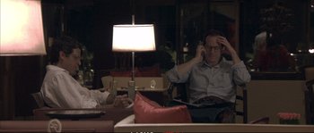 Movie still from “A Mighty Heart” (2007), directed by Michael Winterbottom – A man sitting on a couch talking on the phone; Medium shot, Over the shoulder angle
