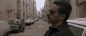 Movie still from “A Mighty Heart” (2007), directed by Michael Winterbottom – A man with a mustache wearing sunglasses on a city street; Close Up shot, Low angle