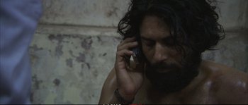 Movie still from “A Mighty Heart” (2007), directed by Michael Winterbottom – A man talking on a cell phone while holding a cell phone to his ear; Close Up shot, High angle
