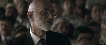 Movie still from “A Mighty Heart” (2007), directed by Michael Winterbottom – An older man with a beard and glasses; Close Up shot, Over the shoulder angle