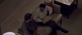 Movie still from “A Mighty Heart” (2007), directed by Michael Winterbottom – Two men sitting on a couch looking at a pillow; Medium shot, High angle