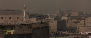 Movie still from “A Mighty Heart” (2007), directed by Michael Winterbottom – A person sitting on top of a brick building; Extreme Wide shot, High angle