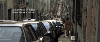 Movie still from “A Mighty Heart” (2007), directed by Michael Winterbottom – A woman walking down a street past parked cars; Wide shot, Over the shoulder angle
