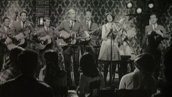 Movie still from “A Mighty Wind” (2003), directed by Christopher Guest – A black and white photo of a group of people singing; Medium shot, High angle