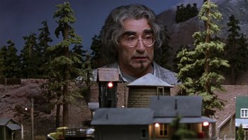 Movie still from “A Mighty Wind” (2003), directed by Christopher Guest – A man's face in front of a model house; Medium shot, Low angle