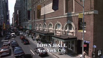 Movie still from “A Mighty Wind” (2003), directed by Christopher Guest – A city street with a large building on the corner; Extreme Wide shot, High angle