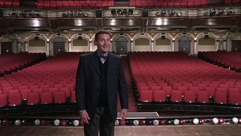 Movie still from “A Mighty Wind” (2003), directed by Christopher Guest – A man standing in front of an empty auditorium; Wide shot, High angle