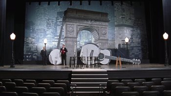 Movie still from “A Mighty Wind” (2003), directed by Christopher Guest – A stage set with chairs and a stage with a guitar on it; Extreme Wide shot, High angle