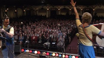 Movie still from “A Mighty Wind” (2003), directed by Christopher Guest – A crowd of people sitting in front of a microphone; Wide shot, Low angle