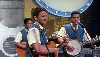 Movie still from “A Mighty Wind” (2003), directed by Christopher Guest – A group of men playing instruments and singing; Medium shot, Over the shoulder angle