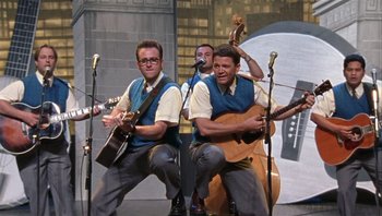 Movie still from “A Mighty Wind” (2003), directed by Christopher Guest – A group of men playing musical instruments on a stage; Wide shot, Low angle