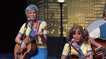 Movie still from “A Mighty Wind” (2003), directed by Christopher Guest – A couple of women are singing and playing guitars; Medium shot, Low angle