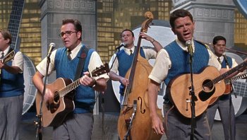 Movie still from “A Mighty Wind” (2003), directed by Christopher Guest – A group of men playing musical instruments on a stage; Medium shot, Low angle