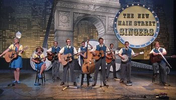 Movie still from “A Mighty Wind” (2003), directed by Christopher Guest – A group of men and women playing musical instruments on a stage; Wide shot, Low angle