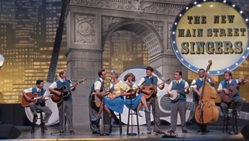 Movie still from “A Mighty Wind” (2003), directed by Christopher Guest – A group of men and a woman on a stage with guitars; Wide shot, Low angle