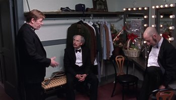 Movie still from “A Mighty Wind” (2003), directed by Christopher Guest – Two men in tuxedos sitting on a bench in a room; Medium shot, Over the shoulder angle