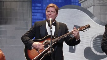 Movie still from “A Mighty Wind” (2003), directed by Christopher Guest – A man in a tuxedo holding a guitar and a microphone; Medium shot, Over the shoulder angle