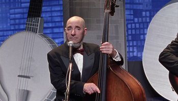 Movie still from “A Mighty Wind” (2003), directed by Christopher Guest – A man in a suit and bow tie holding a double bass; Medium shot, Over the shoulder angle