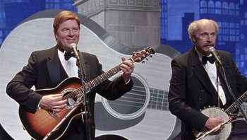 Movie still from “A Mighty Wind” (2003), directed by Christopher Guest – A man in a suit and tie playing a guitar; Medium shot, Over the shoulder angle