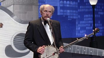 Movie still from “A Mighty Wind” (2003), directed by Christopher Guest – A man in a suit holding a banjo on a stage; Medium shot, Low angle