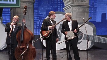Movie still from “A Mighty Wind” (2003), directed by Christopher Guest – A couple of men in suits playing musical instruments on a stage; Wide shot, High angle