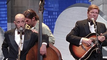 Movie still from “A Mighty Wind” (2003), directed by Christopher Guest – Three men in suits and ties are playing a musical instrument; Medium shot, Over the shoulder angle