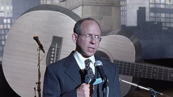 Movie still from “A Mighty Wind” (2003), directed by Christopher Guest – A man in a suit and tie holding a microphone; Close Up shot, Over the shoulder angle