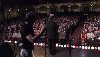 Movie still from “A Mighty Wind” (2003), directed by Christopher Guest – Two men on a stage in front of an audience; Wide shot, High angle
