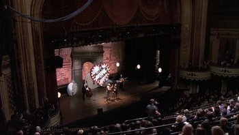 Movie still from “A Mighty Wind” (2003), directed by Christopher Guest – An audience is sitting on a stage and a band is playing; Extreme Wide shot, High angle