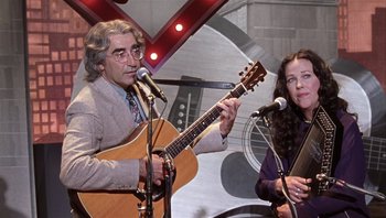 Movie still from “A Mighty Wind” (2003), directed by Christopher Guest – A man and a woman sing into microphones; Medium shot, Low angle