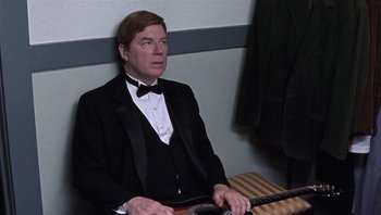 Movie still from “A Mighty Wind” (2003), directed by Christopher Guest – A man in a tuxedo sitting in front of an electric guitar; Medium shot, Low angle