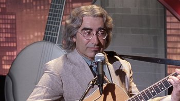 Movie still from “A Mighty Wind” (2003), directed by Christopher Guest – A man in a suit is playing a guitar; Close Up shot, High angle