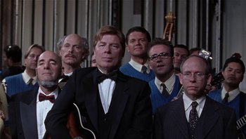 Movie still from “A Mighty Wind” (2003), directed by Christopher Guest – A group of men standing next to each other holding a guitar; Medium shot, Low angle