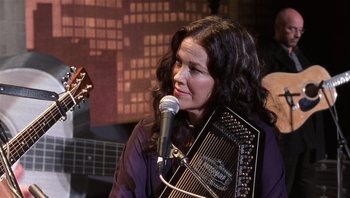 Movie still from “A Mighty Wind” (2003), directed by Christopher Guest – A woman with long black curly hair holding an instrument; Close Up shot, Over the shoulder angle