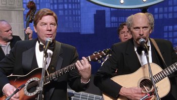 Movie still from “A Mighty Wind” (2003), directed by Christopher Guest – A man in a tuxedo is playing a guitar while others watch; Medium shot, Low angle