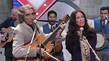 Movie still from “A Mighty Wind” (2003), directed by Christopher Guest – A man and a woman sing and a man plays a guitar; Medium shot, Over the shoulder angle