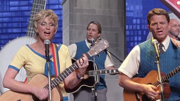 Movie still from “A Mighty Wind” (2003), directed by Christopher Guest – A group of people singing and playing guitars; Medium shot, Low angle