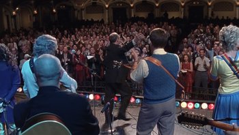 Movie still from “A Mighty Wind” (2003), directed by Christopher Guest – A group of people on a stage with a microphone; Wide shot, Low angle