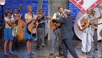 Movie still from “A Mighty Wind” (2003), directed by Christopher Guest – A group of people on a stage playing music; Wide shot, Over the shoulder angle