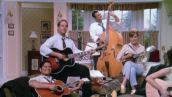 Movie still from “A Mighty Wind” (2003), directed by Christopher Guest – A group of men and women playing musical instruments in a living room; Wide shot, Low angle