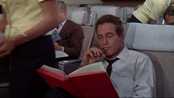 Movie still from “A New Kind of Love” (1963), directed by Melville Shavelson – A man sitting on a seat reading a book; Medium shot, High angle