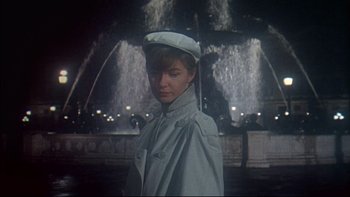 Movie still from “A New Kind of Love” (1963), directed by Melville Shavelson – A woman wearing a white hat standing in front of a fountain at night; Medium shot, Low angle