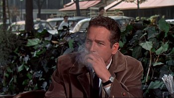 Movie still from “A New Kind of Love” (1963), directed by Melville Shavelson – A man smoking a cigarette while sitting in a park; Medium shot, Low angle
