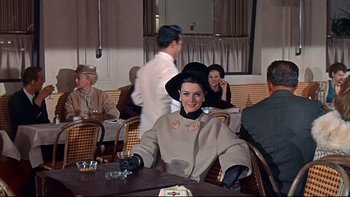 Movie still from “A New Kind of Love” (1963), directed by Melville Shavelson – A woman sitting at a table in front of a group of people; Medium shot, High angle