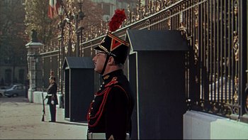 Movie still from “A New Kind of Love” (1963), directed by Melville Shavelson – A man in a uniform stands in front of a fence; Wide shot, Low angle