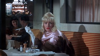 Movie still from “A New Kind of Love” (1963), directed by Melville Shavelson – A woman sitting at a table smoking a cigarette; Medium shot, Over the shoulder angle